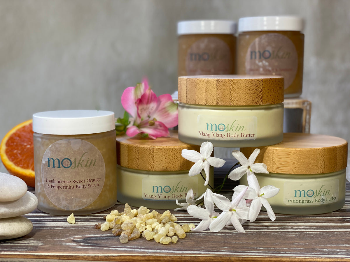 Hands patting legs dry with a towel after a shower, then warming a small scoop of body butter in the palms before applying to towel‑damp skin.