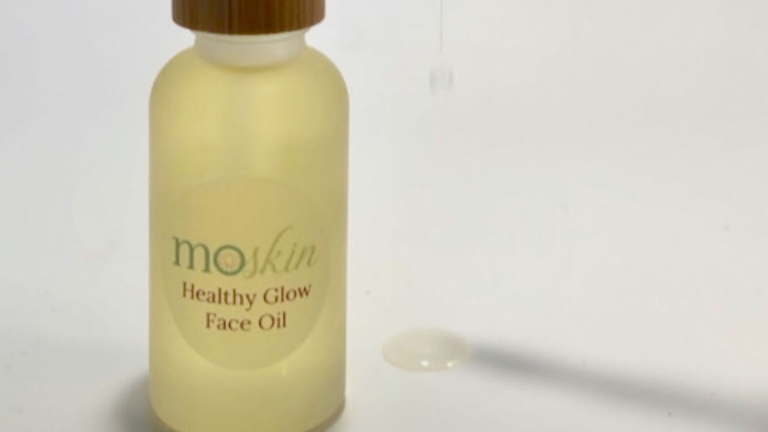 A small amber bottle of facial oil beside a travel pouch, passport, and reusable cotton rounds—shot in soft morning light.