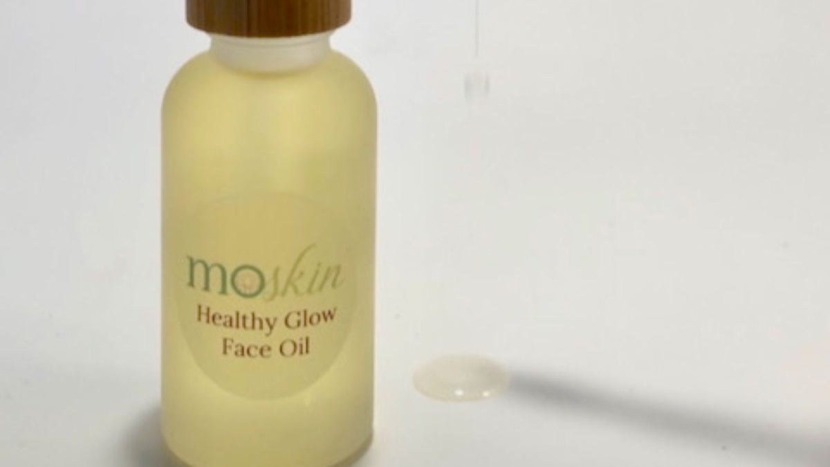 A small amber bottle of facial oil beside a travel pouch, passport, and reusable cotton rounds—shot in soft morning light.
