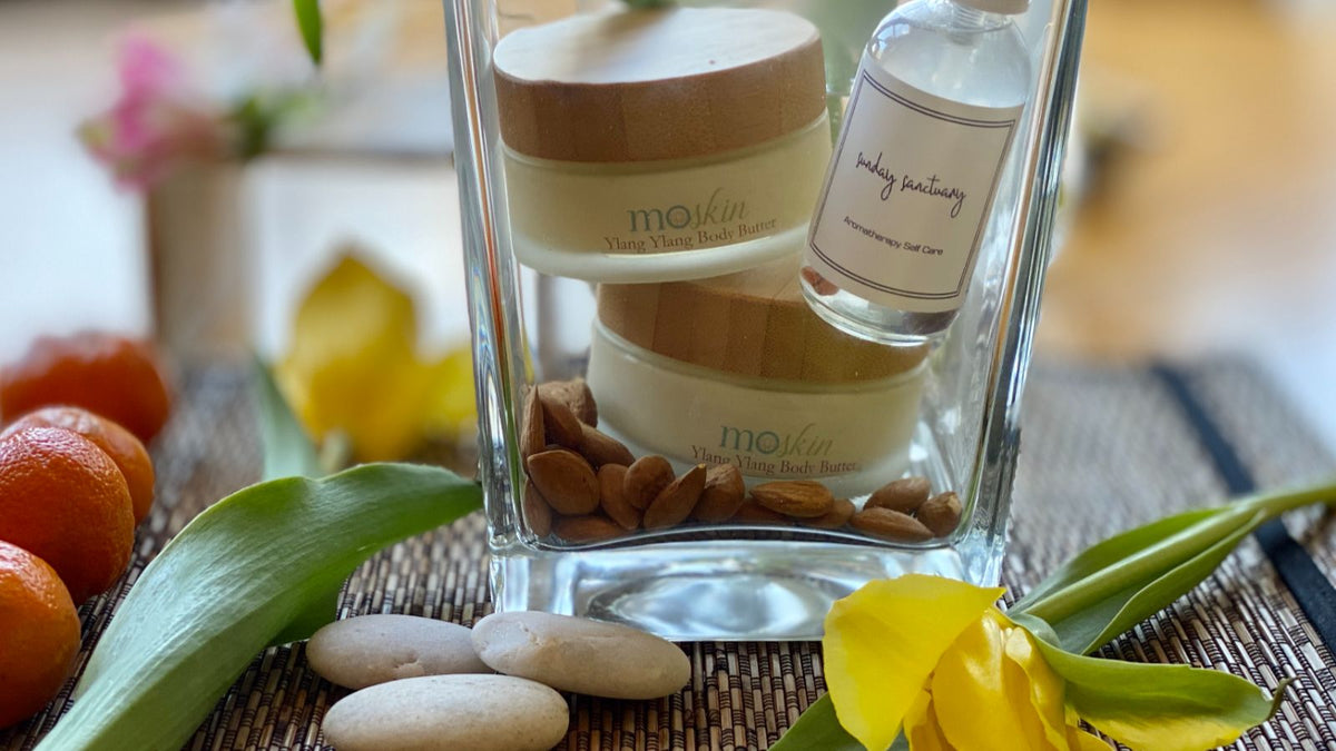 A small dollop of unscented cream mixing with a pea-size amount of aromatic body butter in a palm, next to dried citrus and herbs—showing a simple at‑home dilution technique.